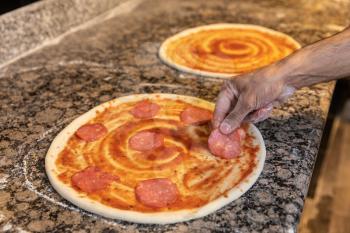 Pizza cooking, man putting sausage on the dough
