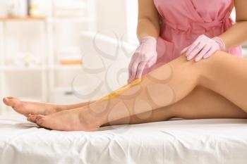 Woman having hair removal procedure on leg with sugaring paste in salon�