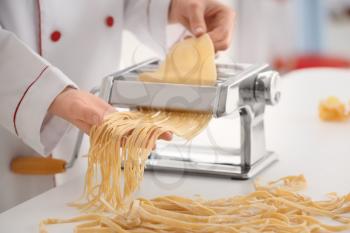 Female chef making noodles with pasta machine at table�