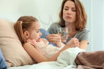 Young woman giving pill for her ill daughter in bed�
