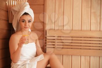Young beautiful woman drinking cold water with lemon in sauna�