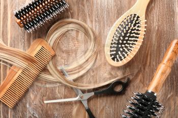 Flat lay composition with hairdresser's tools and strand of blonde hair on wooden background�