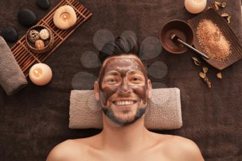 Young man with face mask on massage table in spa salon�