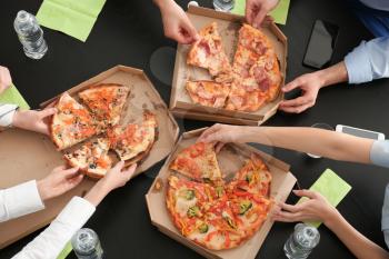 Young people eating pizza at table in office, top view�