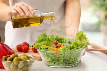 Woman dressing fresh vegetable salad with olive oil in kitchen�