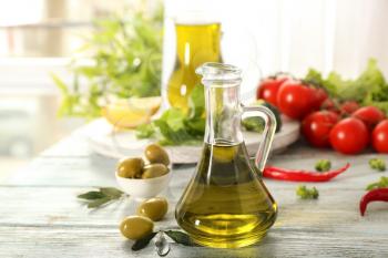 Glass jug with fresh olive oil on wooden table�