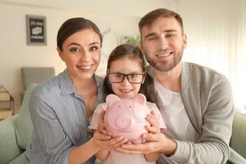 Happy little girl with her parents  holding piggy bank indoors. Money savings concept�
