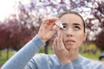Young woman using eye drops near blooming trees. Allergy concept�