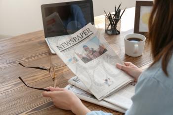 Young woman reading newspaper at table indoors�