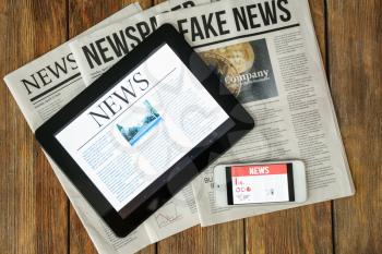 Newspapers, tablet computer and phone with news on screen on wooden table�