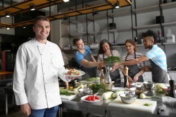 Handsome male chef holding plate with prepared dish during cooking classes�