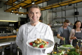 Handsome male chef holding plate with prepared dish during cooking classes�