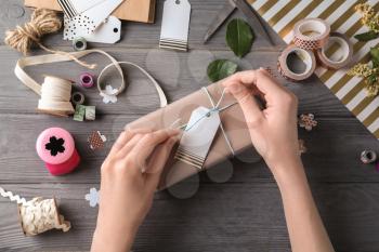 Woman packing beautiful gift on wooden background�