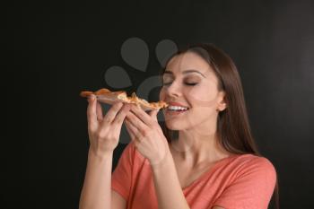 Young woman eating slice of hot tasty pizza on dark background�