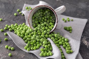 Cup with delicious fresh green peas on grey textured background�
