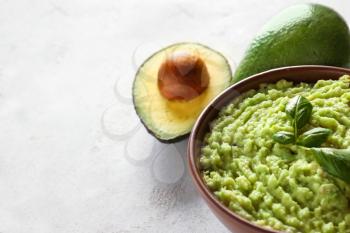 Bowl with tasty guacamole and ripe avocados on light textured background�