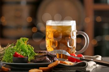 Mug of delicious beer with grilled steak and sauce on table�