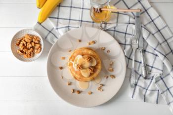 Plate with tasty pancakes, walnuts and sliced banana on table�