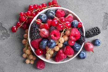 Bowl with different ripe berries on grey table�