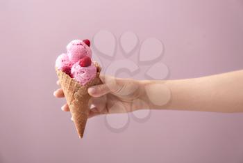 Woman holding waffle cone with delicious raspberry ice-cream on color background�