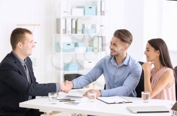 Young man shaking hands with estate agent in office�