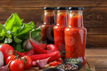 Bottles with tasty sauces and vegetables on wooden table�