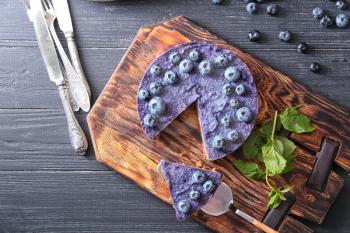 Board with tasty blueberry cheesecake on wooden table�
