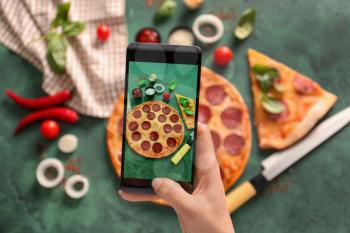 Woman taking photo of tasty Pepperoni pizza on table�