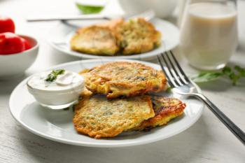 Plate with zucchini pancakes and sauce on wooden table�