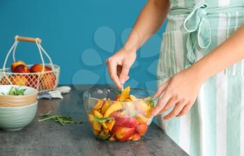 Woman preparing tasty salad with sliced peaches and arugula�