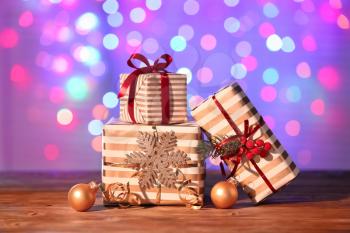 Beautiful Christmas gift boxes with decorations on table against blurred lights�