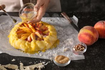 Woman smearing raw peach galette with egg yolk at table�