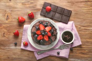 Plate with tasty chocolate pancakes and berries on wooden table�