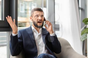 Emotional businessman talking on phone in office�