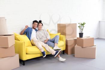 Happy interracial couple resting on sofa near carton boxes in room. Moving into new house�