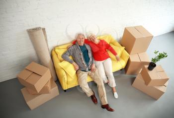 Mature couple sitting on sofa near boxes after moving into new house�