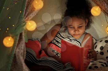 Little African-American girl reading bedtime story in hovel�
