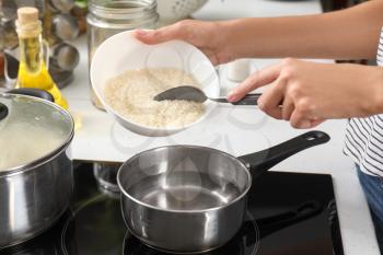 Woman pouring raw rice into saucepan with boiling water on stove�