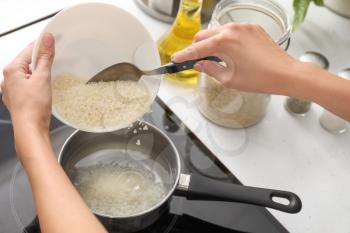 Woman pouring raw rice into saucepan with boiling water on stove�