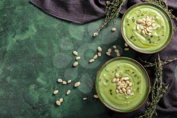 Bowls with tasty zucchini soup and peanuts on color background�