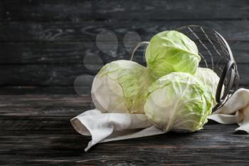 Overturned metal basket with fresh cabbages on wooden table�