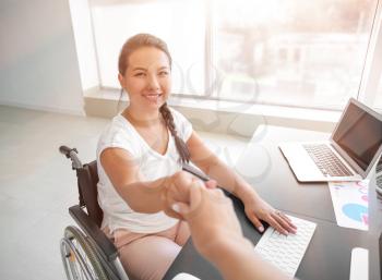 Businesswoman in wheelchair shaking hands with colleague in office�