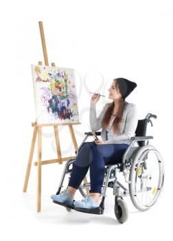 Young female artist in wheelchair painting picture on white background�