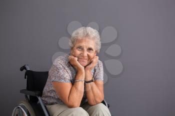 Senior woman in wheelchair on grey background�