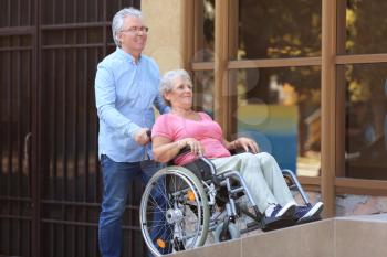 Senior woman in wheelchair and her husband on ramp outdoors�