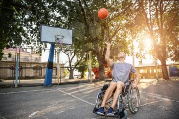 Young man in wheelchair playing basketball outdoors�
