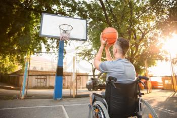 Young man in wheelchair playing basketball outdoors�