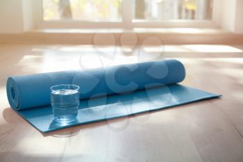 Yoga mat and glass of water on floor indoors�