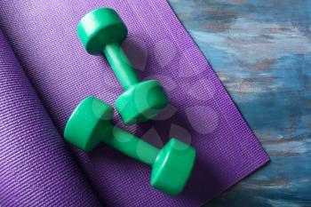 Yoga mat with dumbbells on wooden background�
