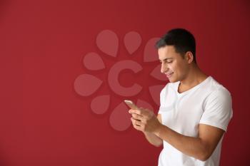 Young man with mobile phone on color background�
